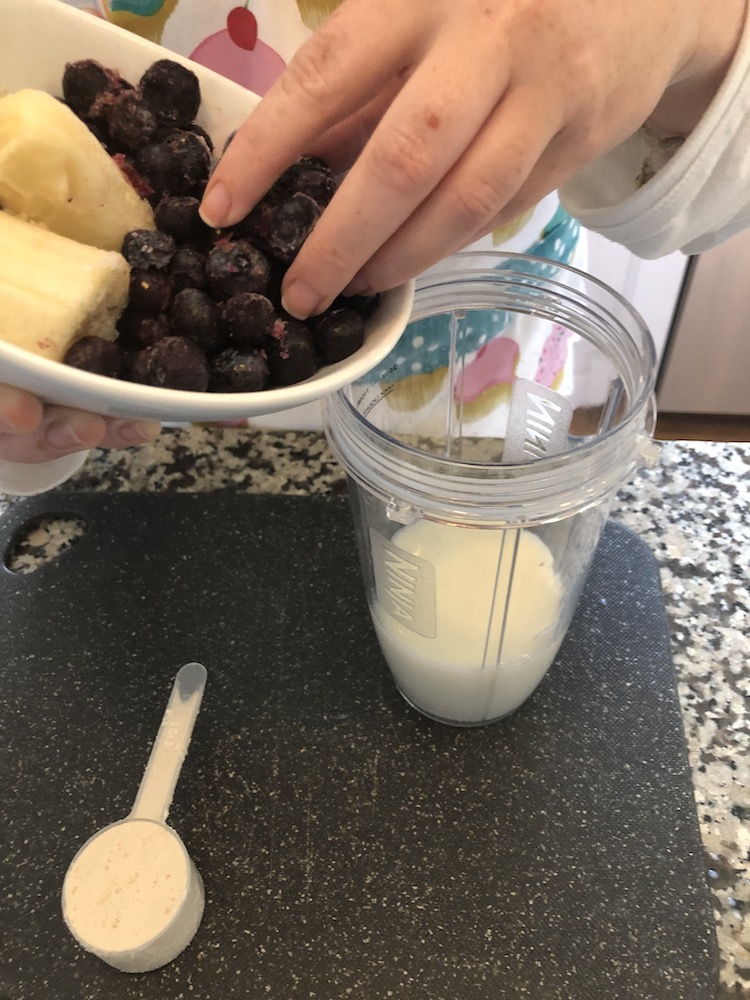 woman adding blueberries to a blender to make a protein shake