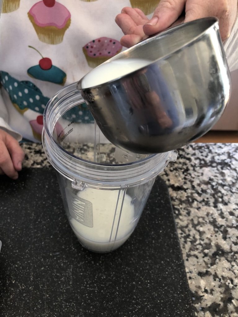 woman pouring milk in blender to make protein shake