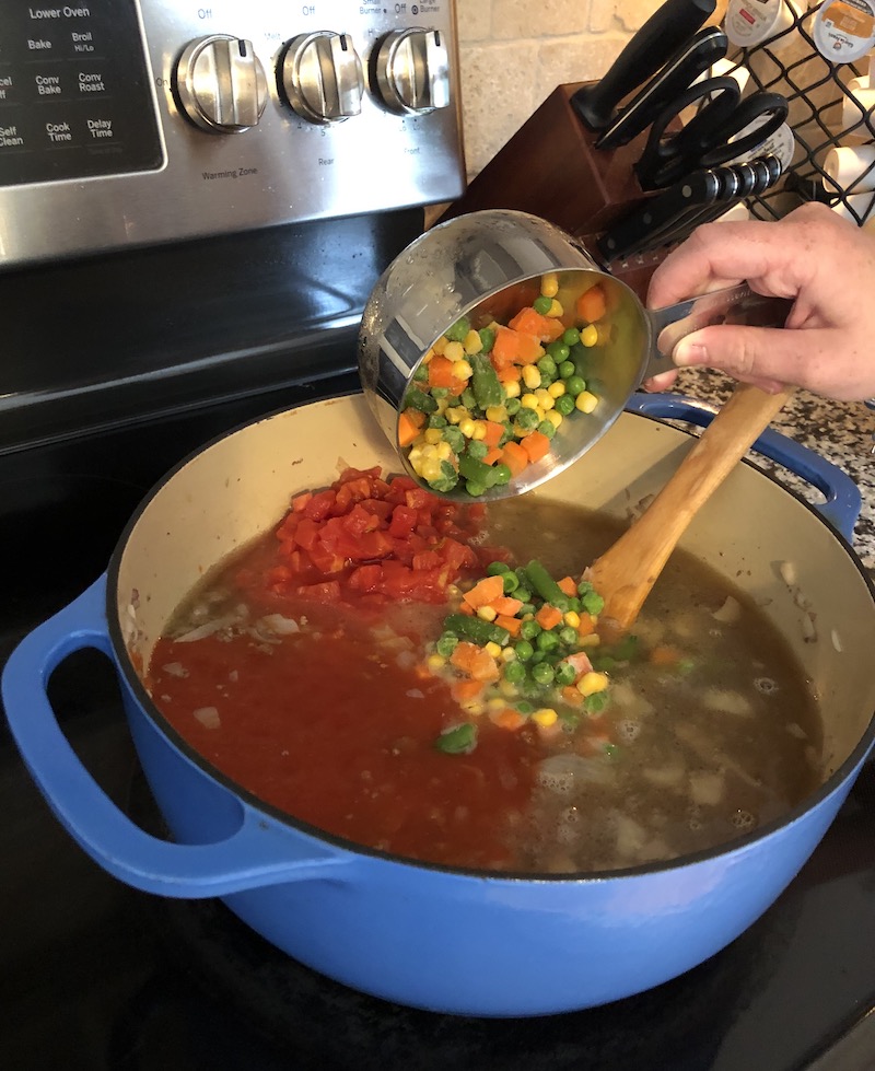 Woman adding healthy mixed vegetables to soup

